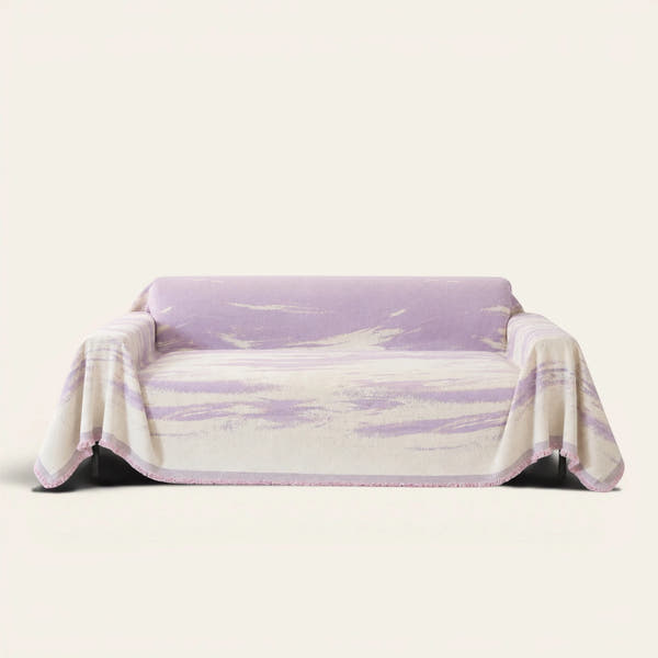 Lavender Drift Brushwave Chenille sofa throw draped over a two-seat sofa, front view on ivory background, pink fringed hem