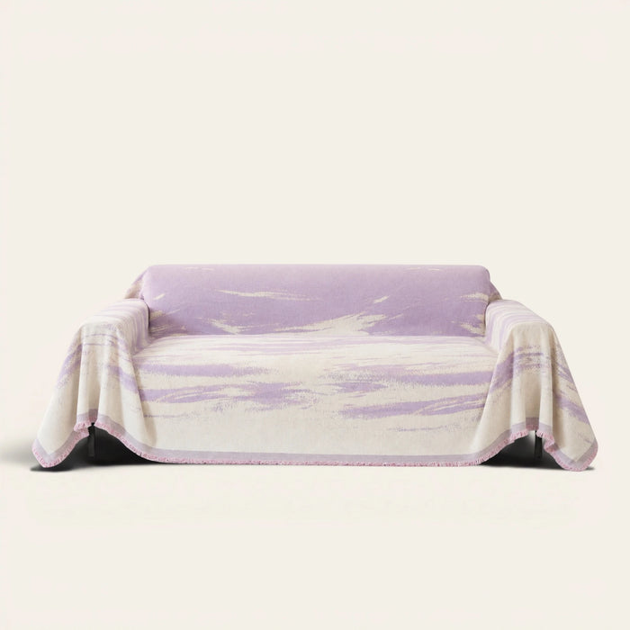 Lavender Drift Brushwave Chenille sofa throw draped over a two-seat sofa, front view on ivory background, pink fringed hem