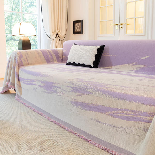 Lavender Drift Brushwave Chenille throw styled on a sofa with a scalloped cushion and floor lamp by a window