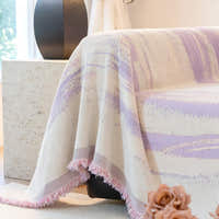 Lavender Drift Brushwave Chenille throw cascading over a sofa corner, fringed pink edge beside a black vase