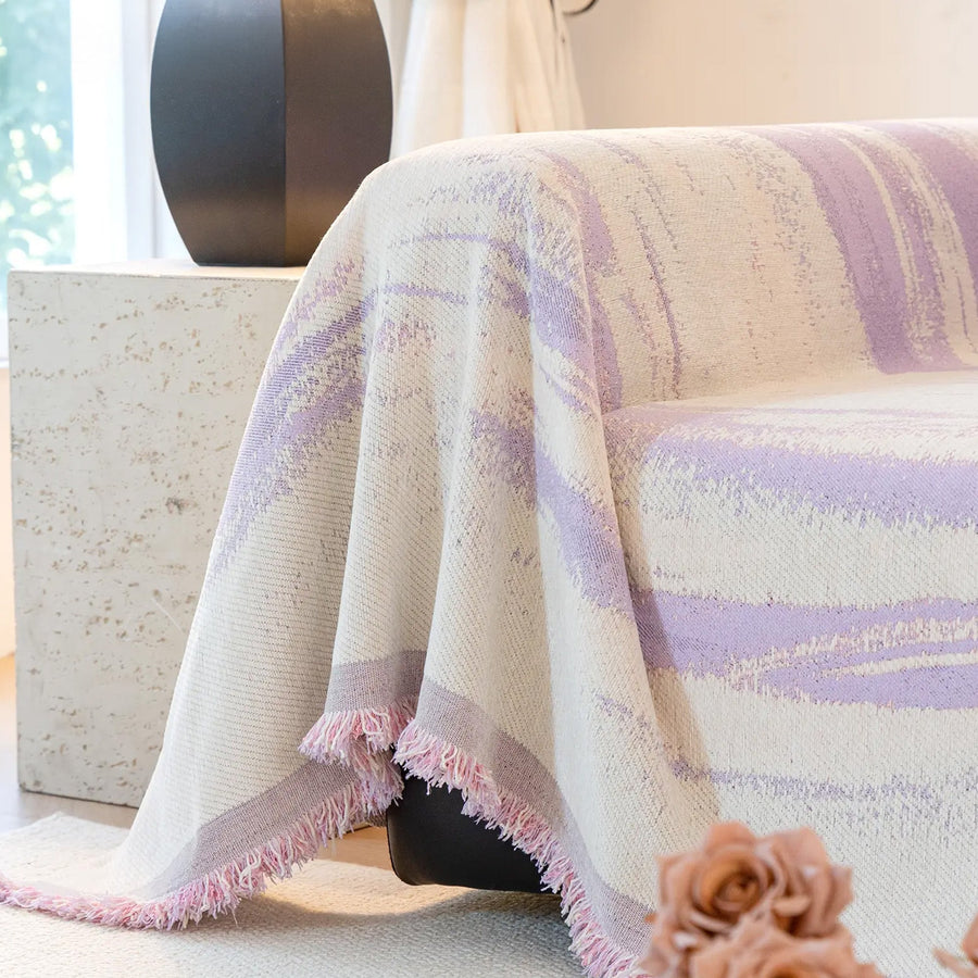 Lavender Drift Brushwave Chenille throw cascading over a sofa corner, fringed pink edge beside a black vase