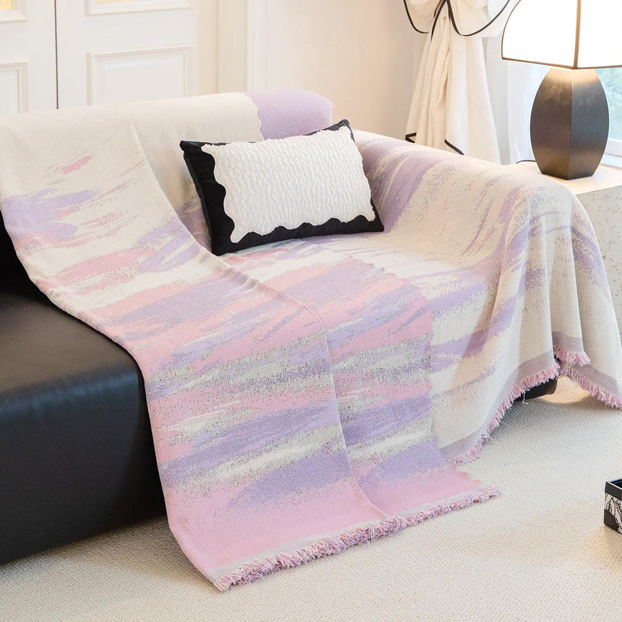 Lavender Drift Brushwave Chenille throw draped over the arm of a black leather sofa, flowing to the floor