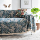 Angled view of the Blue Bouquet throw on a sofa beside a fiddle-leaf plant and framed art