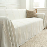 Ivory Whisper Classic Striped throw draped across a sofa seat and armrest, angled view with window light and cushion