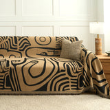 Angled view of the Contemporary Tribal ebony sand throw over a sofa with a woven cushion and lamp