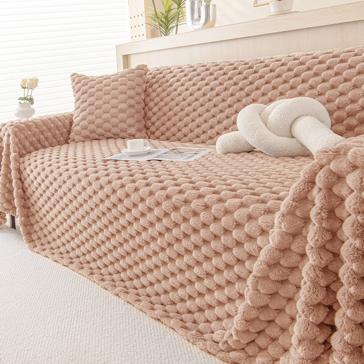 Blush Pink plush throw styled on a sofa with a matching cushion, knot pillow and cup