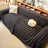 Charcoal Gray Cozy Houndstooth throw on a sofa with line-art cushion and knot ball, angled view by wood shelving