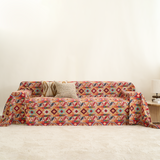 Colorful crimson boho throw covering a sofa with knit cushion and lamp in a warm room