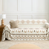 Beige Geometry Geometric Boho throw styled on a sofa against a paneled wall with a lamp and cushion