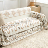 Beige Geometry boho throw covering a couch in a bright room with a knit cushion and rattan lamp