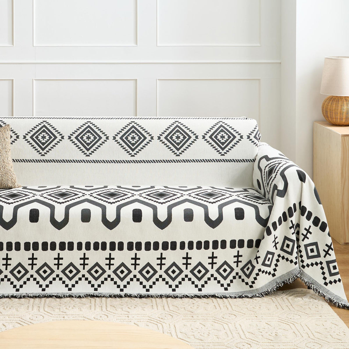 Black Geometry boho throw styled on a sofa against a paneled wall with a knit cushion and rattan lamp