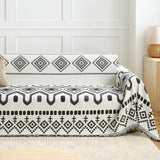 Black Geometry boho throw styled on a sofa against a paneled wall with a knit cushion and rattan lamp