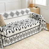 Black Geometry boho throw covering a couch with a knit cushion and rattan lamp on a woven rug