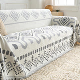 Gray Geometry Geometric Boho throw draped across a sofa arm and seat, three-quarter view with fringe
