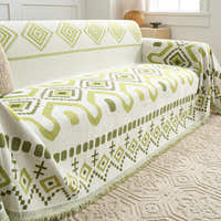 Green Geometry Geometric Boho throw draped over a sofa arm and seat, three-quarter view with fringe
