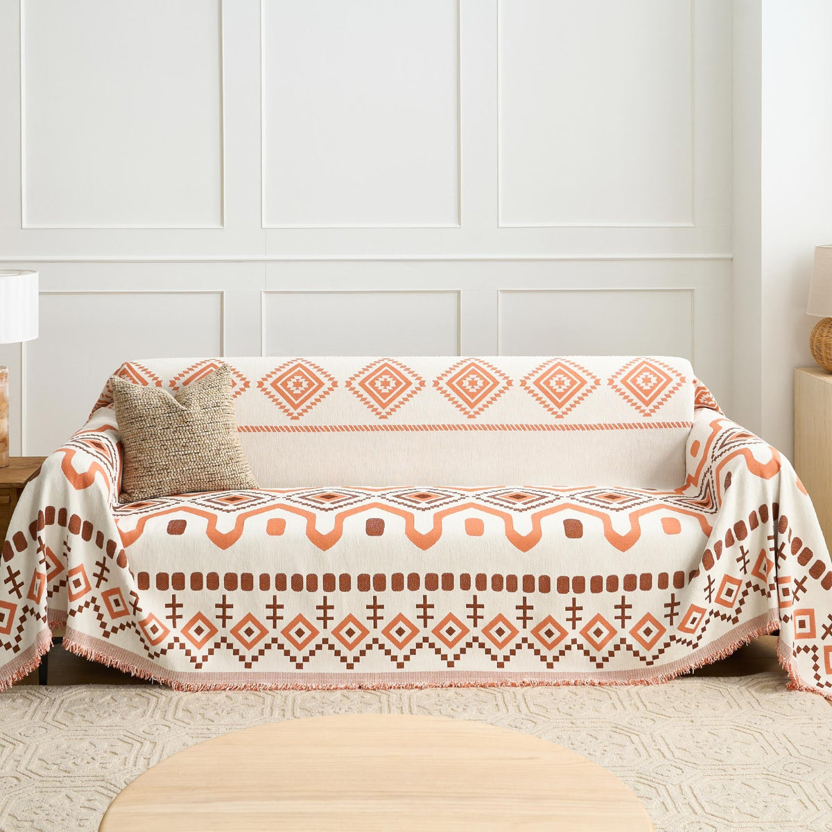 Geometric boho throw covering a couch by a panelled wall with jute cushion and lamp