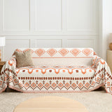 Geometric boho throw covering a couch by a panelled wall with jute cushion and lamp