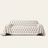 Geometric Chenille sofa throw in Black Boba over a couch, front view with black polka dots and fringe