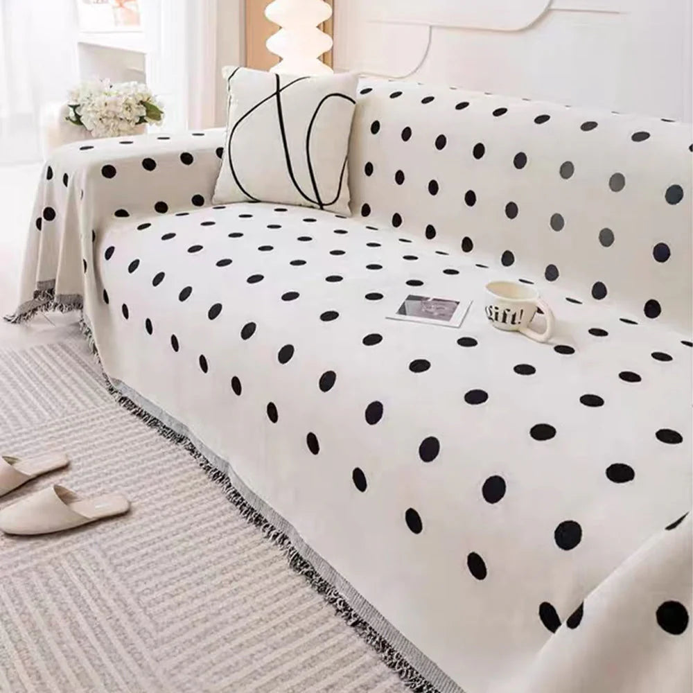Black Boba polka dot throw draped on an L-shaped sofa with a line-art cushion, mug and slippers