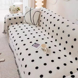 Black Boba throw covering a sofa with a line-art cushion, magazine and mug beside a ribbed lamp