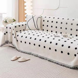 Wider view of the Black Boba polka dot throw on a couch with a cushion, mug and slippers
