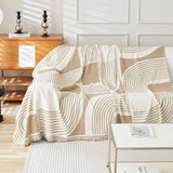 Brown Stream Geometric Harmony throw draped over a sofa beside a wood console, angled view with fringe detail