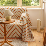 Orange Arrow chevron throw draped over a sofa corner beside a wooden lamp table in a bright room