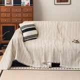Charcoal Stripe Linear Weave throw over a sofa with a folded striped cushion, angled view by a wood cabinet