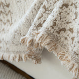 Detail of the cream latte Luxe Heritage throw's fringed, tasseled edge draping over the sofa