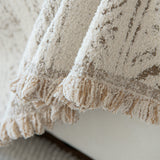 Close-up of the tufted texture and tasseled fringe of the pearl beige throw