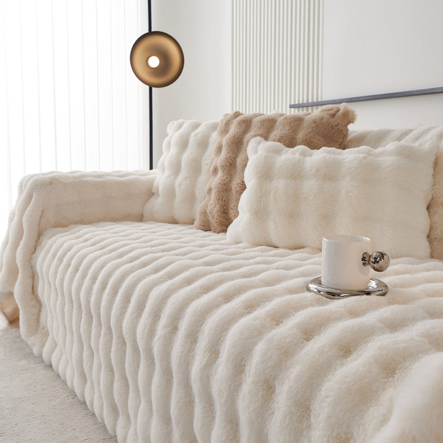 Ivory Luxe faux fur throw on a sofa with plush cushions and a cup, close angle view