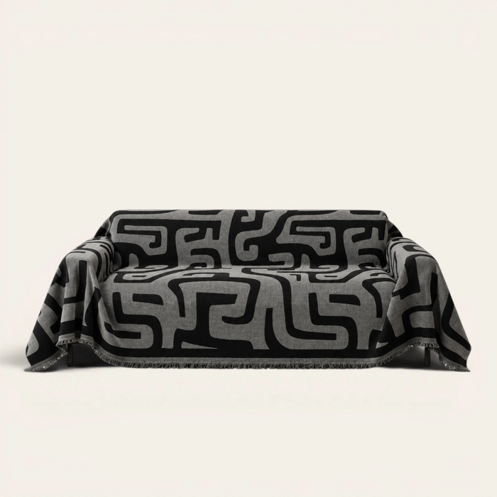 Charcoal Mist Modern Maze sofa throw draped over a three seater sofa, front view on ivory background with fringe