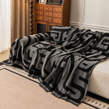Charcoal Mist Modern Maze throw cascading over a sofa back, angled view beside a wood cabinet and curtain