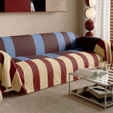 Angled view of the Brick Blue Modern Striped throw on a sofa beside a glass table and lamp