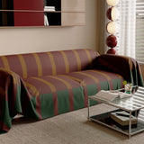 Brick Olive Modern Striped throw draped over a sofa near a bright window, angled view with glass side table
