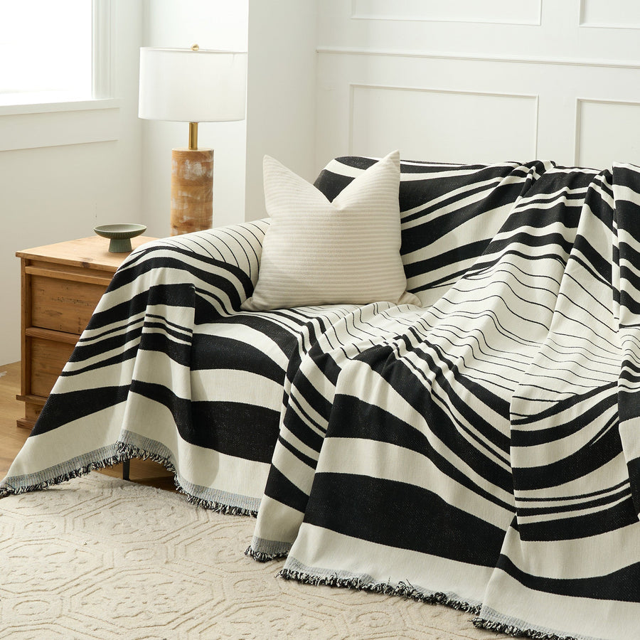 Modern Wave throw draped over a sofa corner beside a wood nightstand and lamp