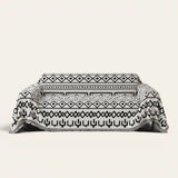 Sleek Boho sofa throw in Black Bohemia over a couch, front view with monochrome tribal pattern and fringe