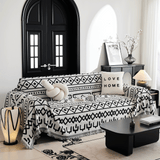 Angled view of the Black Bohemia throw draped on a sofa beside a cabinet, vase and floor lamp