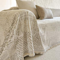 Sand beige mosaic throw draped over a sofa arm with fringe and beige cushions
