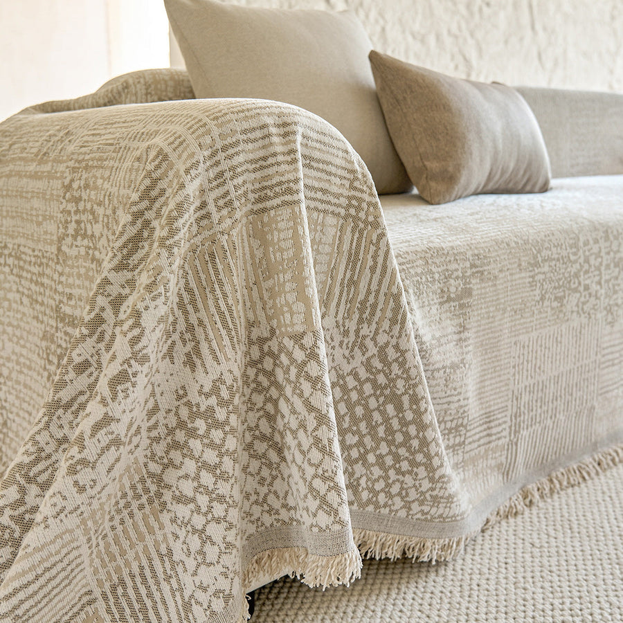 Sand beige mosaic throw draped over a sofa arm with fringe and beige cushions