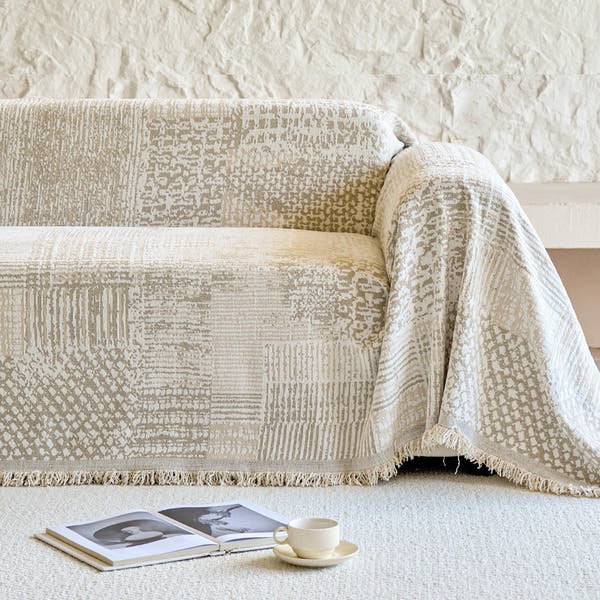 Sand beige mosaic throw covering a sofa against a rustic stone wall with open book
