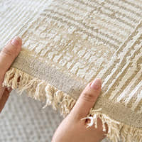 Hands holding the sand beige mosaic fabric showing woven texture and fringed edge