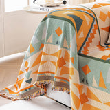 Close-up of the tribal sunset amber sage geometric sofa throw draped over a sofa arm, fringed edge and geometric weave