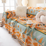 Tribal Sunset amber sage geometric sofa throw covering a full sofa, styled with a flower cushion in a sunlit room